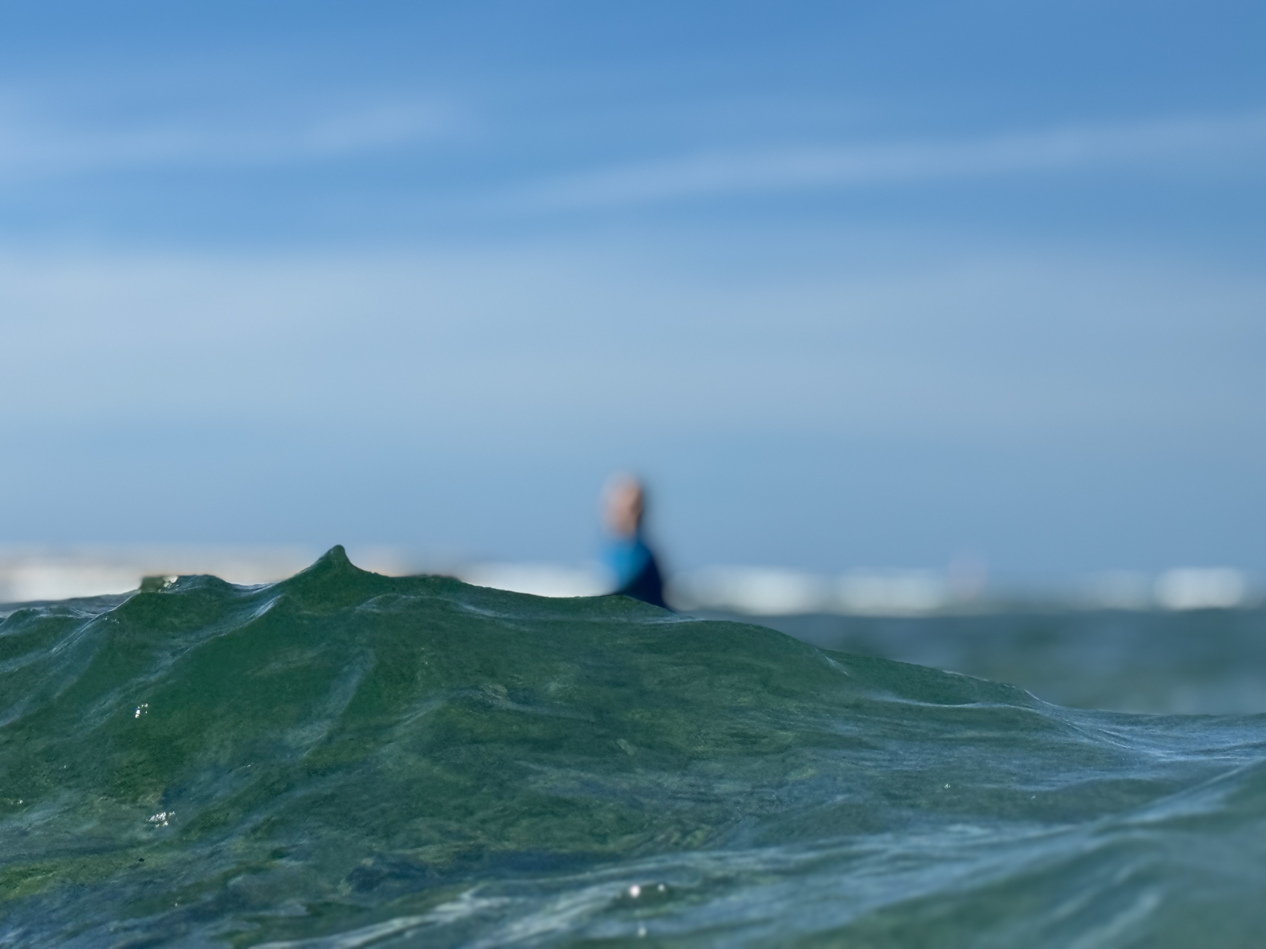 Underwater POV of a green wave with a surfer behind it